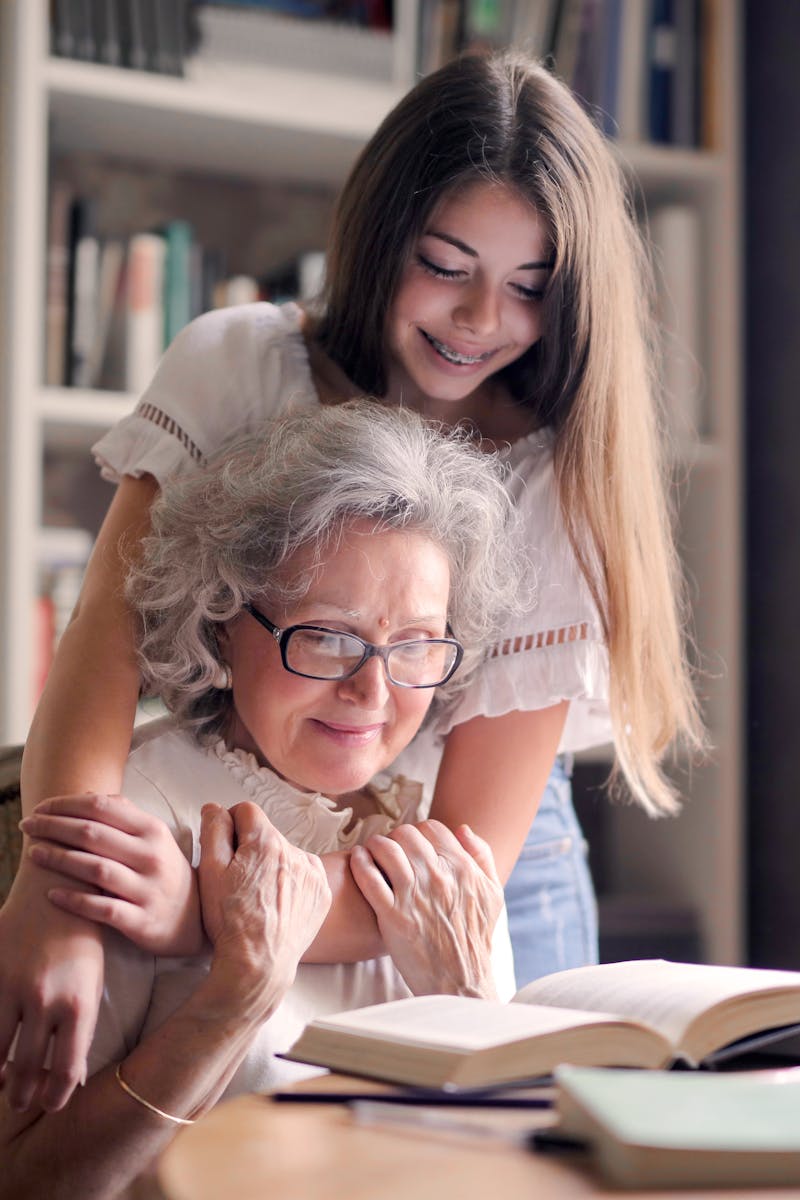 A heartwarming moment of a granddaughter embracing her grandmother as she reads a book together indoors.